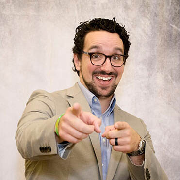 energetic man with glasses and curly hair, pointing at camera